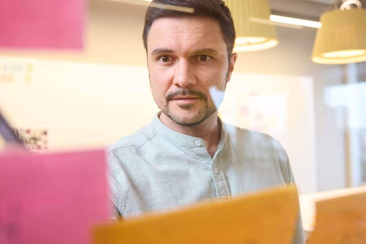 Mann im Büro beim Brainstorming für New Work Ideen, umgeben von bunten Notizzetteln am Glas.