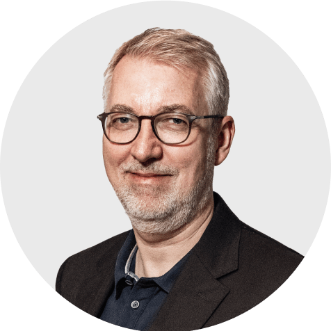 Portr&auml;t von Michael Schmitz, Head Business Development bei Scompler, l&auml;chelnd mit Brille vor hellem Hintergrund.