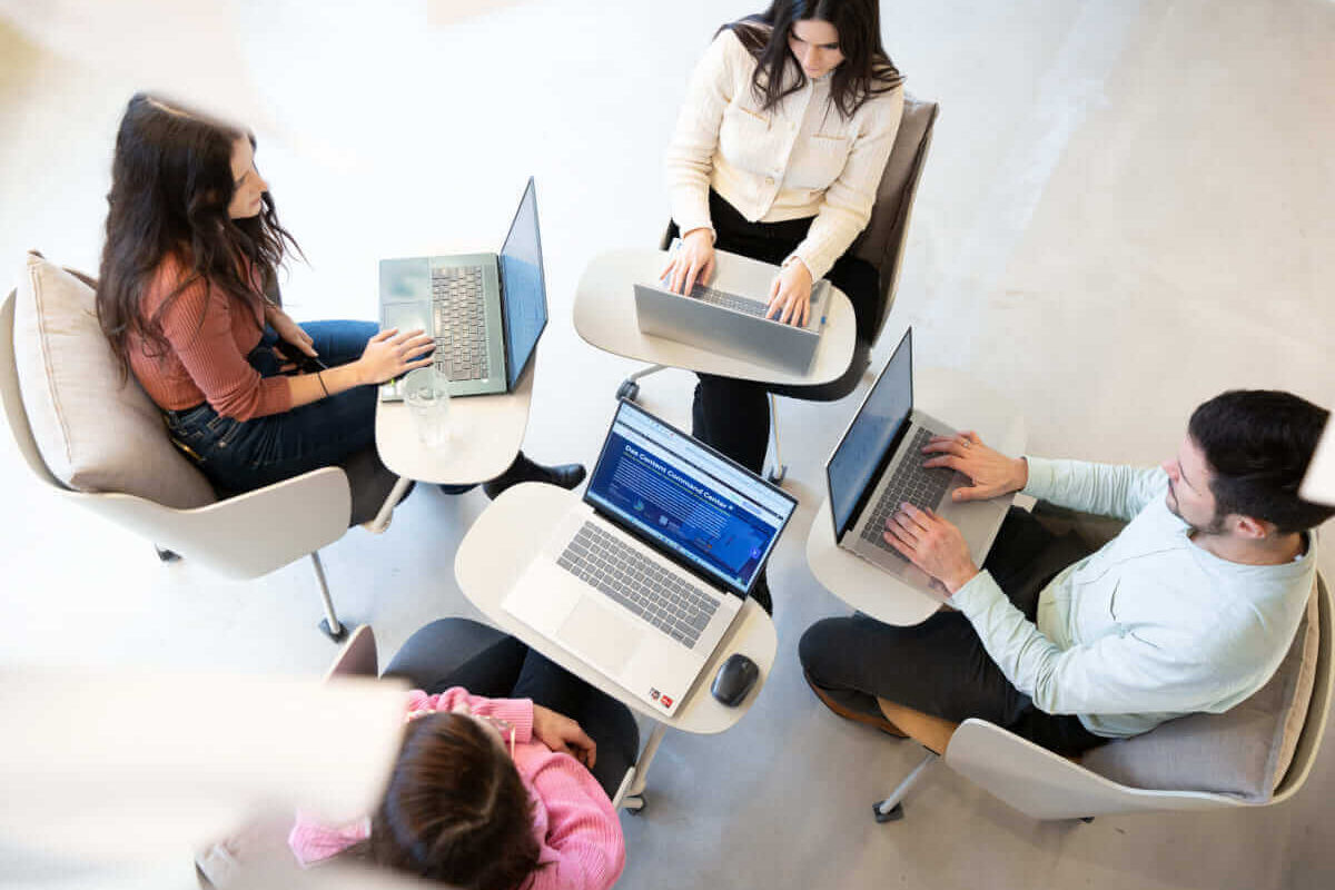 Vier Kollegen arbeiten mit Laptops an einem modernen Arbeitsplatz. Effiziente Teamarbeit in offener Umgebung.