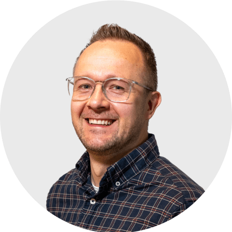 Lachender Toni Liebetrau, Experte von Scompler, mit Brille und kariertem Hemd, blickt optimistisch.